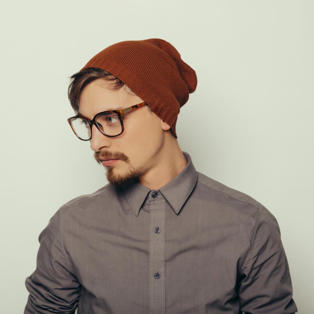 Men’s knit beanie in charcoal with Luvuma logo, displayed on a light color wall background