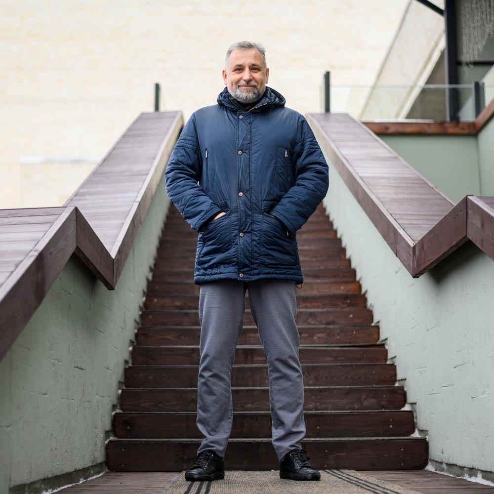 Male athlete wearing a sleek blue jacket, hands in pockets, standing in an urban outdoor setting