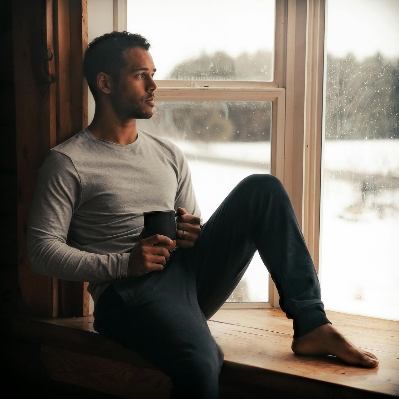 Man sitted on a balcony drinking coffee before workout in long-sleeve performance tee by Luvuma